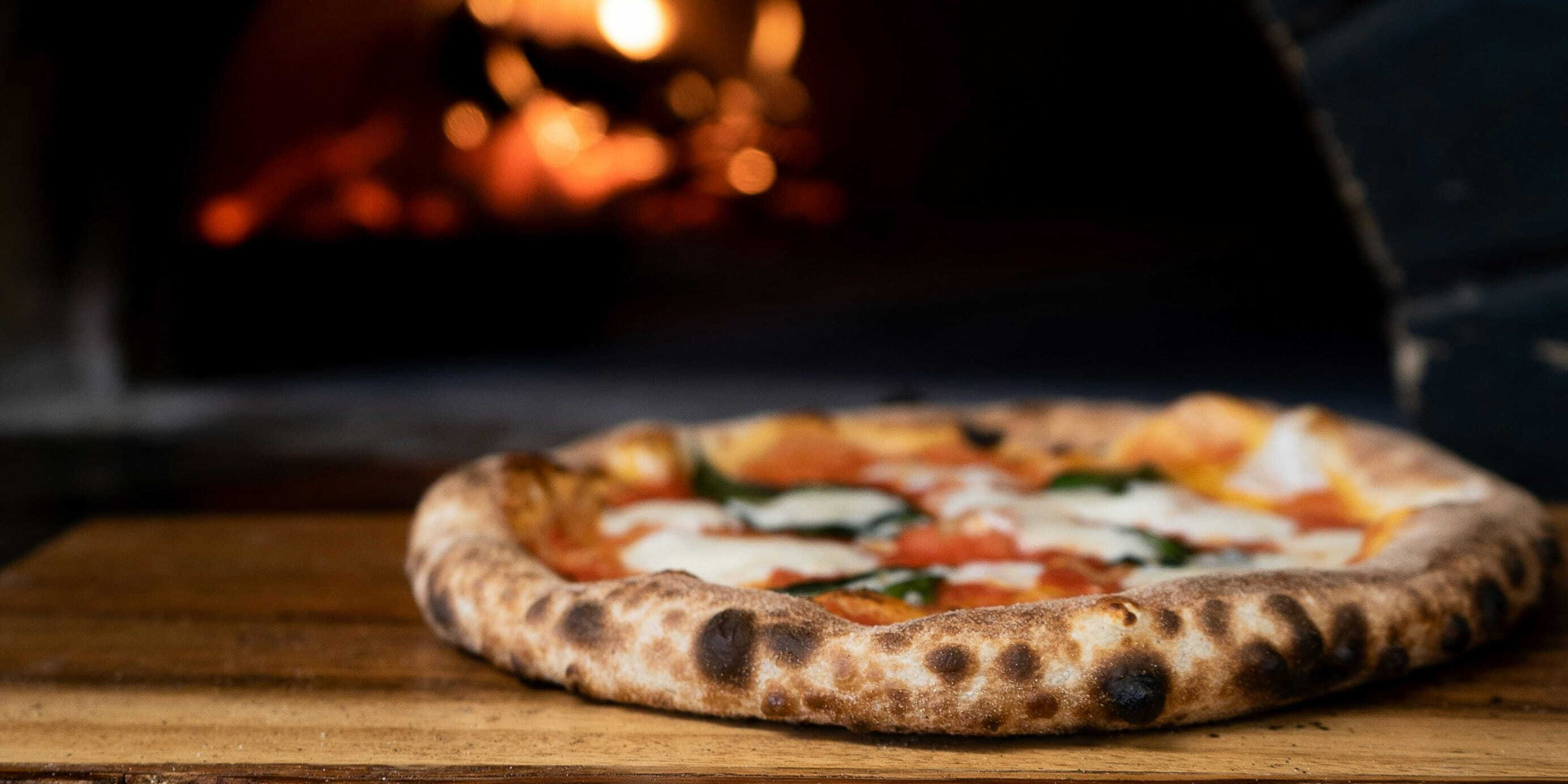 A pizza sits in front of a wood-fired oven