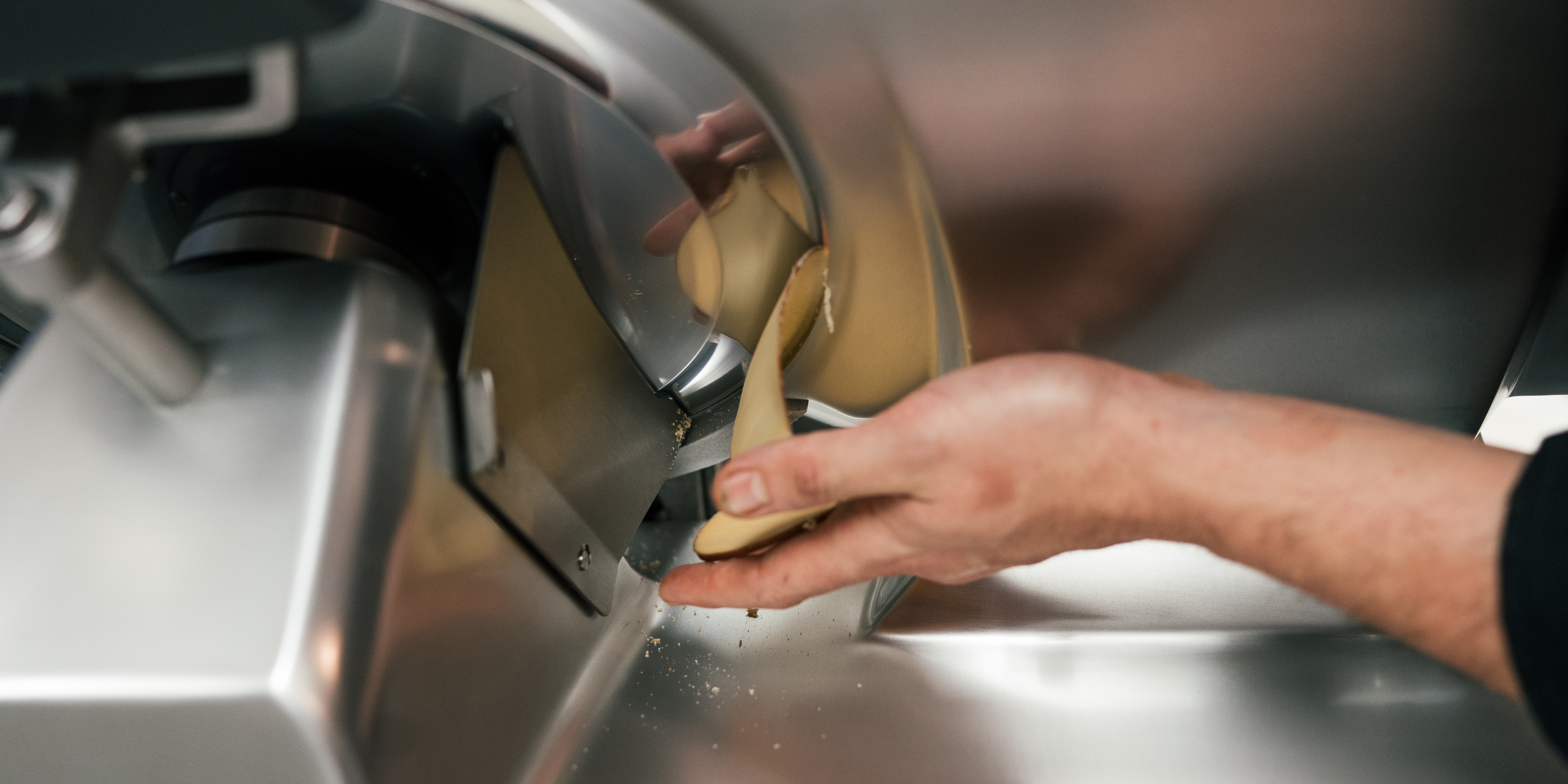 A hand catches meat being sliced on a Centerline by Hobart commericial slicer