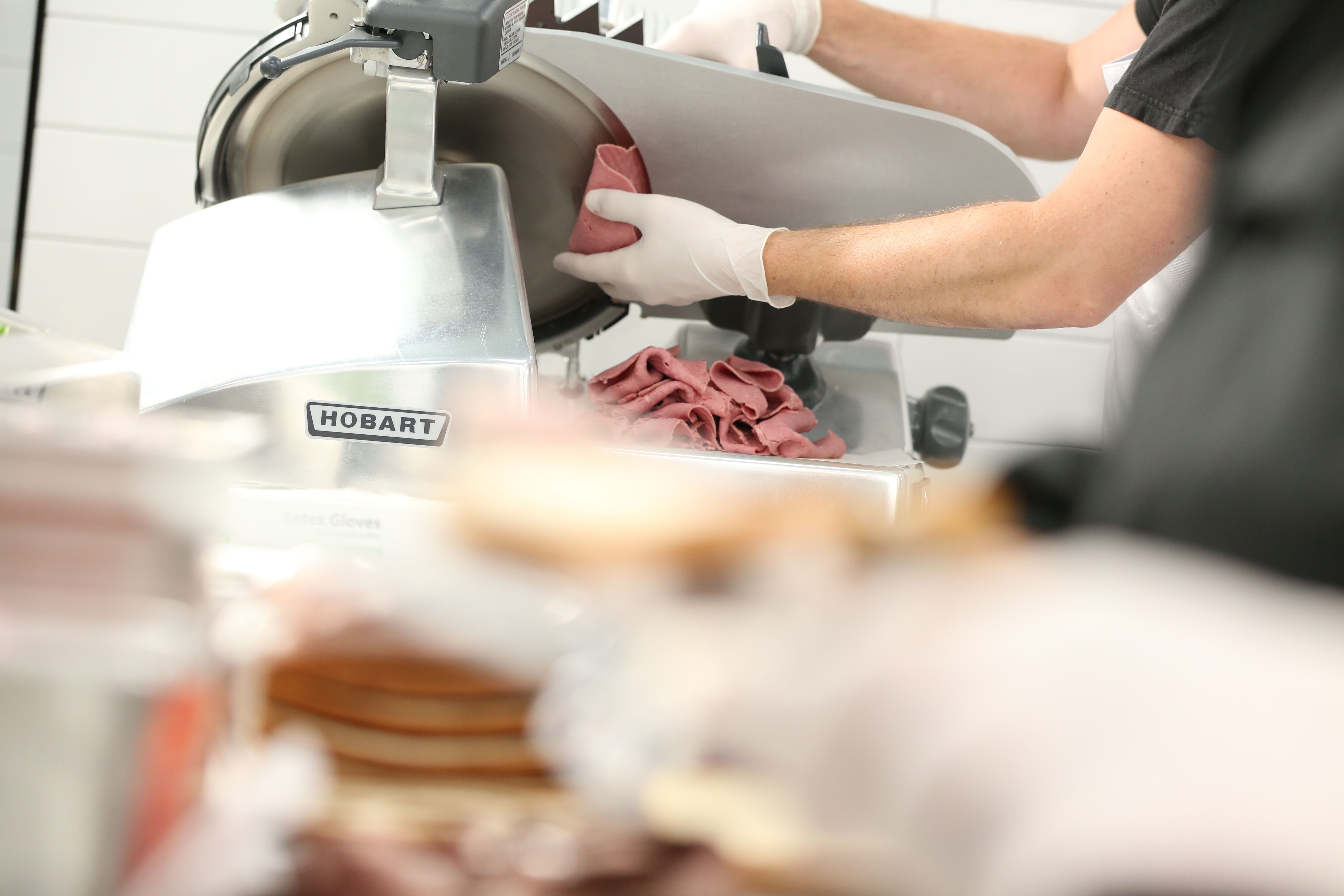 Operator using commercial kitchen slicer with removable blade to slice deli meat. 